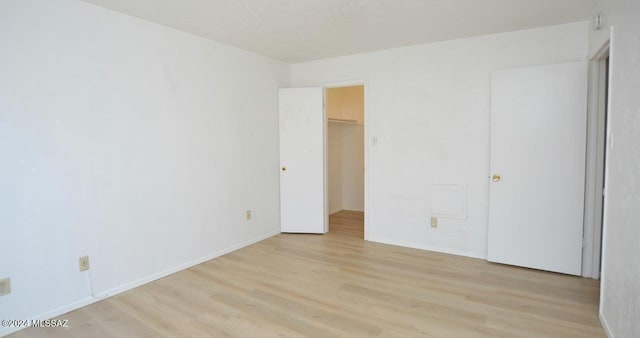 unfurnished bedroom featuring a closet, a walk in closet, and light hardwood / wood-style floors