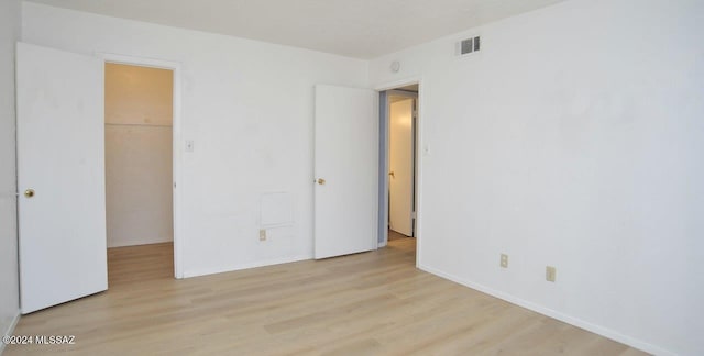 unfurnished bedroom with a spacious closet and light hardwood / wood-style floors