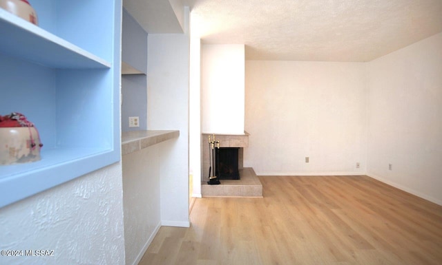 unfurnished living room with a tiled fireplace, light hardwood / wood-style floors, and a textured ceiling