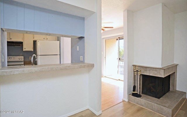 kitchen featuring a tile fireplace, light wood-type flooring, white refrigerator, stove, and ceiling fan