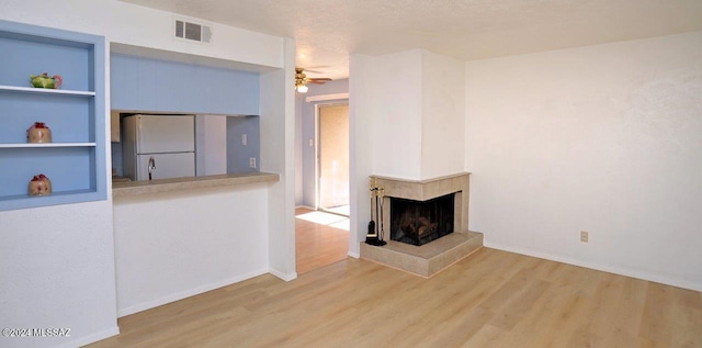 unfurnished living room featuring a multi sided fireplace, a textured ceiling, wood-type flooring, and ceiling fan