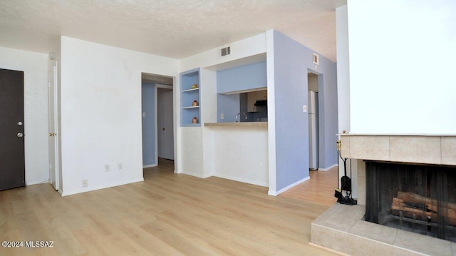 living room featuring a tile fireplace, a textured ceiling, built in shelves, and light hardwood / wood-style floors