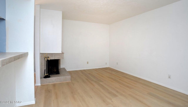 unfurnished living room featuring a tiled fireplace, a textured ceiling, and light wood-type flooring