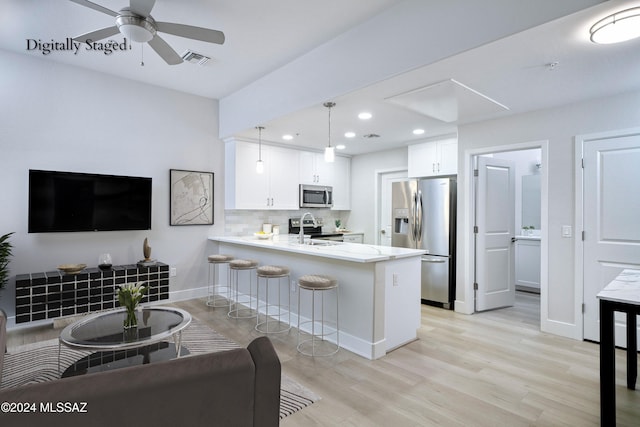 kitchen with stainless steel appliances, light hardwood / wood-style floors, kitchen peninsula, decorative light fixtures, and white cabinets