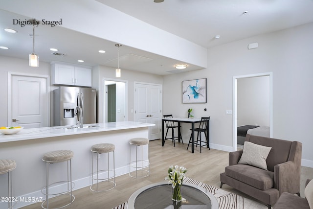 kitchen featuring stainless steel fridge, light wood-type flooring, white cabinetry, pendant lighting, and a breakfast bar