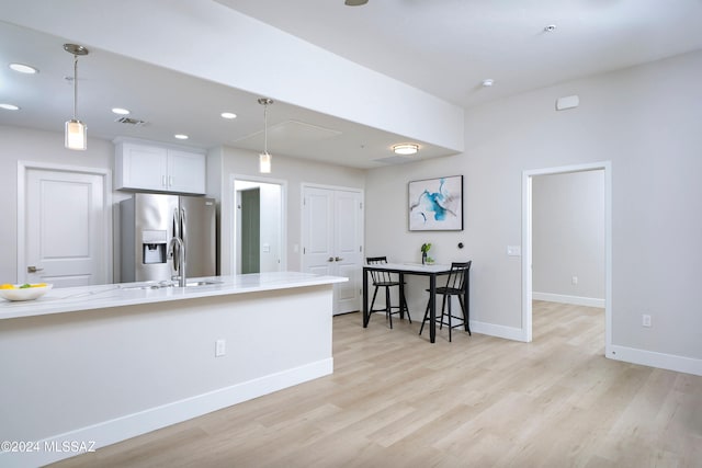 kitchen with white cabinets, light hardwood / wood-style floors, pendant lighting, and stainless steel fridge with ice dispenser