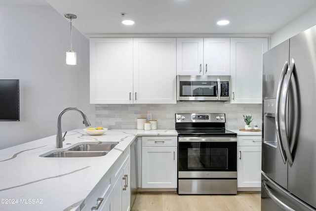 kitchen featuring light stone counters, appliances with stainless steel finishes, pendant lighting, sink, and white cabinets