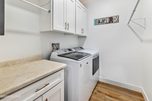 laundry area featuring washer and clothes dryer, light hardwood / wood-style flooring, and cabinets