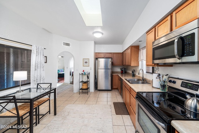 kitchen featuring light tile patterned flooring, a skylight, appliances with stainless steel finishes, and sink