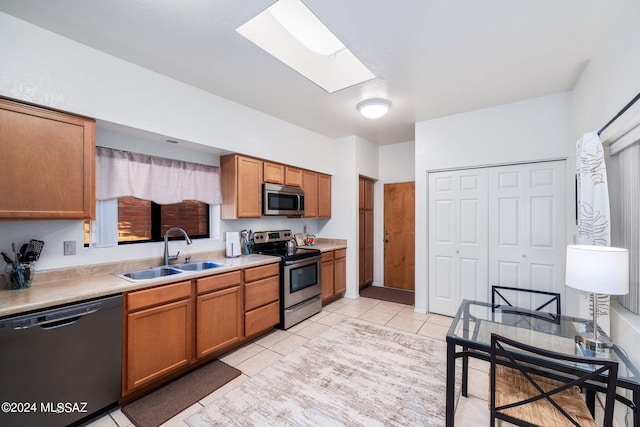 kitchen featuring light tile patterned floors, stainless steel appliances, a skylight, and sink