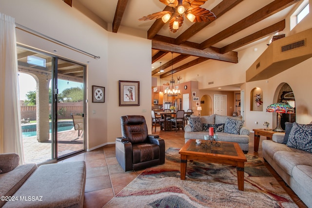 tiled living room with ceiling fan with notable chandelier, beam ceiling, and a high ceiling