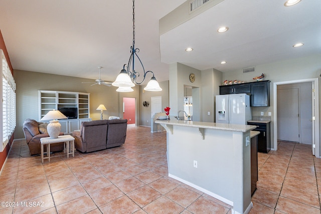 kitchen with a kitchen bar, white refrigerator with ice dispenser, hanging light fixtures, light stone counters, and light tile patterned floors