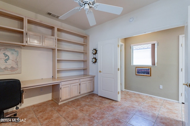 unfurnished office with built in desk, ceiling fan, and light tile patterned flooring