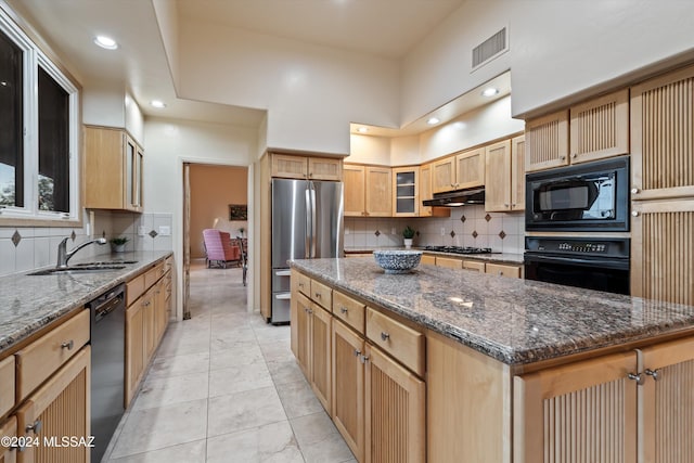 kitchen featuring sink, tasteful backsplash, black appliances, a kitchen island, and dark stone counters