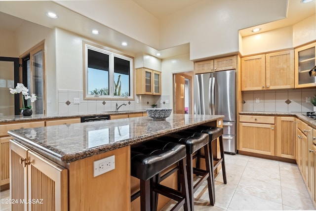 kitchen featuring sink, a breakfast bar, stainless steel refrigerator, a center island, and stone countertops