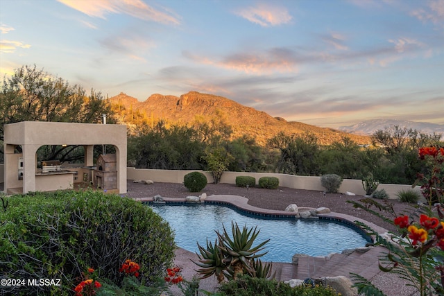 pool at dusk featuring a mountain view, a patio, and an outdoor kitchen