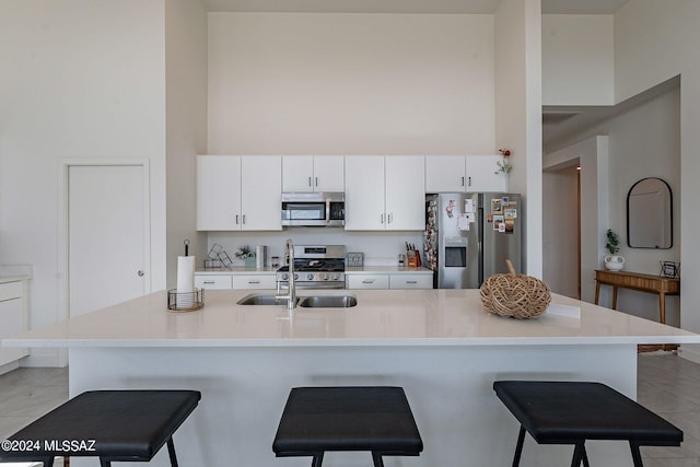 kitchen featuring stainless steel appliances, a breakfast bar, a towering ceiling, and white cabinetry