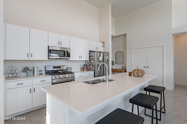 kitchen featuring light tile patterned floors, a breakfast bar, a sink, a towering ceiling, and appliances with stainless steel finishes