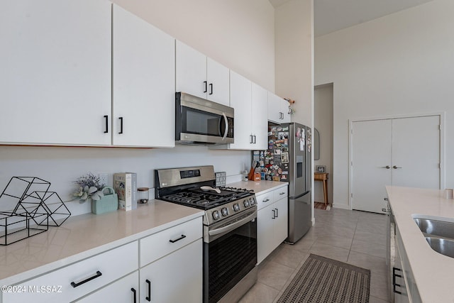 kitchen featuring stainless steel appliances, white cabinets, light countertops, and a towering ceiling