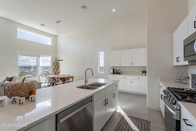 kitchen featuring appliances with stainless steel finishes, a towering ceiling, white cabinets, a kitchen bar, and a center island with sink