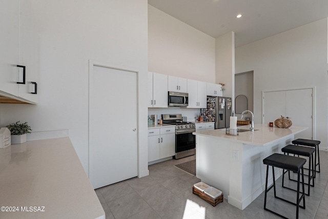 kitchen featuring a breakfast bar, light countertops, a towering ceiling, appliances with stainless steel finishes, and white cabinets