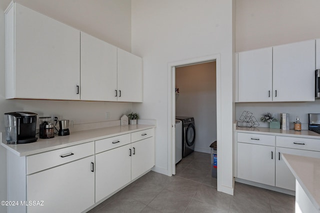 kitchen with light tile patterned floors, a high ceiling, light countertops, washer and dryer, and white cabinetry