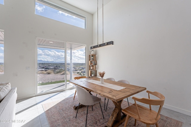 dining space with baseboards, light tile patterned flooring, a towering ceiling, and a healthy amount of sunlight