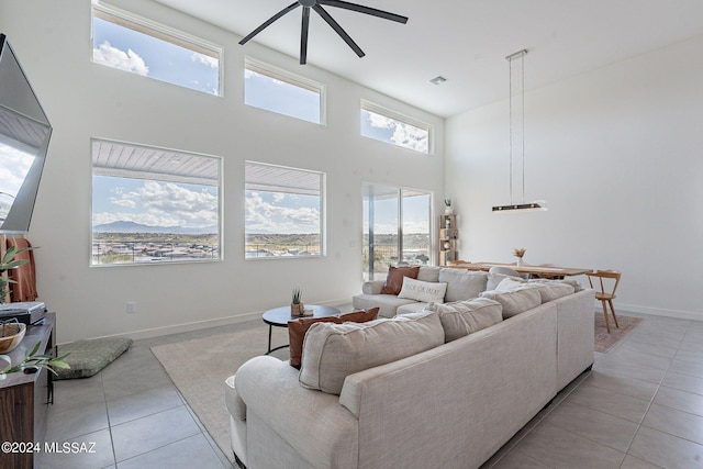 living area featuring light tile patterned flooring, visible vents, a towering ceiling, a ceiling fan, and baseboards