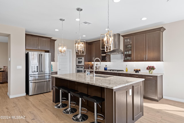 kitchen featuring light hardwood / wood-style floors, stainless steel appliances, wall chimney exhaust hood, and dark brown cabinets