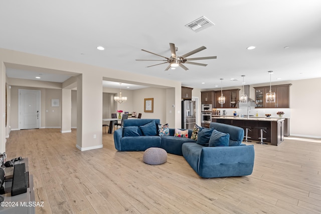 living room featuring light hardwood / wood-style floors, sink, and ceiling fan with notable chandelier