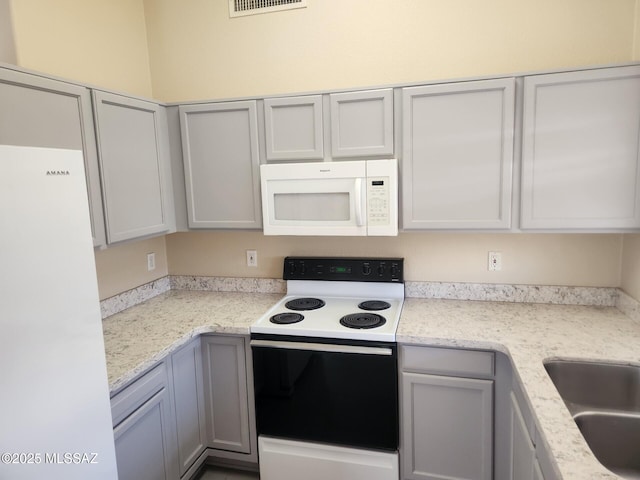 kitchen featuring light stone counters, sink, and white appliances