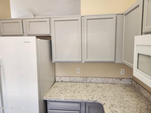 kitchen featuring white refrigerator, light stone counters, and white cabinets