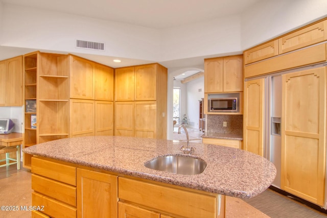 kitchen featuring a kitchen island with sink, light brown cabinetry, oven, and a breakfast bar