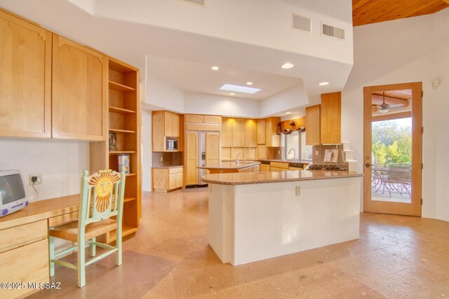 kitchen with sink, light stone counters, tasteful backsplash, built in appliances, and light brown cabinets