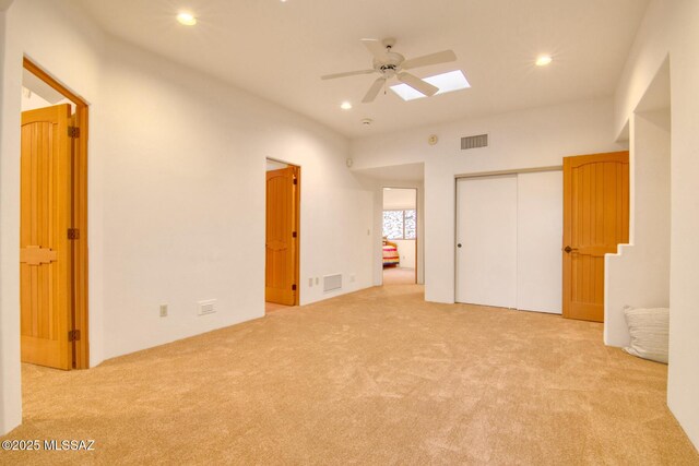 unfurnished bedroom featuring ceiling fan, light colored carpet, a skylight, and a closet