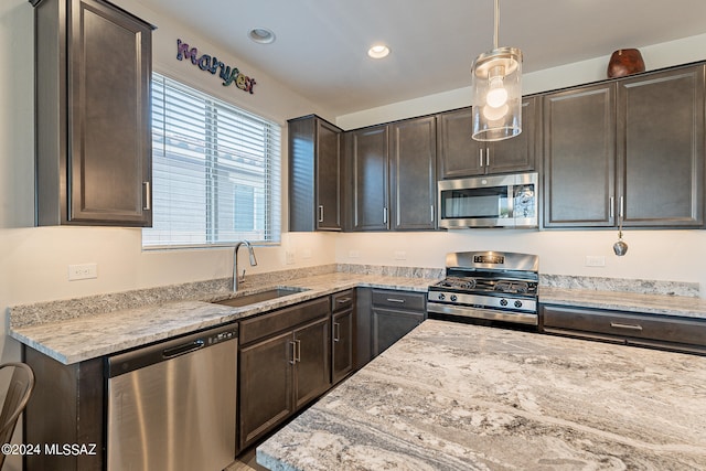 kitchen featuring hanging light fixtures, sink, dark brown cabinetry, appliances with stainless steel finishes, and light stone counters