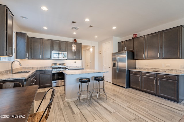 kitchen with appliances with stainless steel finishes, sink, a kitchen island, light hardwood / wood-style floors, and pendant lighting