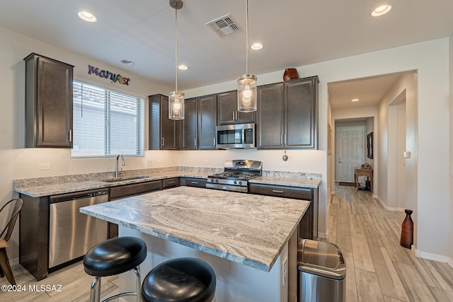 kitchen with appliances with stainless steel finishes, sink, a center island, pendant lighting, and light hardwood / wood-style flooring