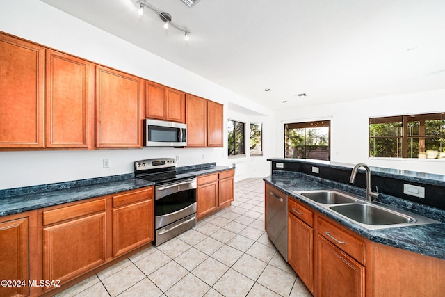 kitchen featuring appliances with stainless steel finishes, light tile patterned flooring, sink, and dark stone counters