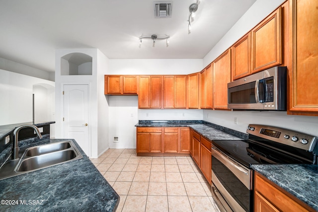 kitchen featuring sink, appliances with stainless steel finishes, dark stone counters, and light tile patterned flooring