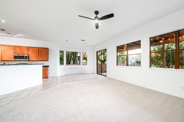 unfurnished living room featuring ceiling fan, light colored carpet, and plenty of natural light