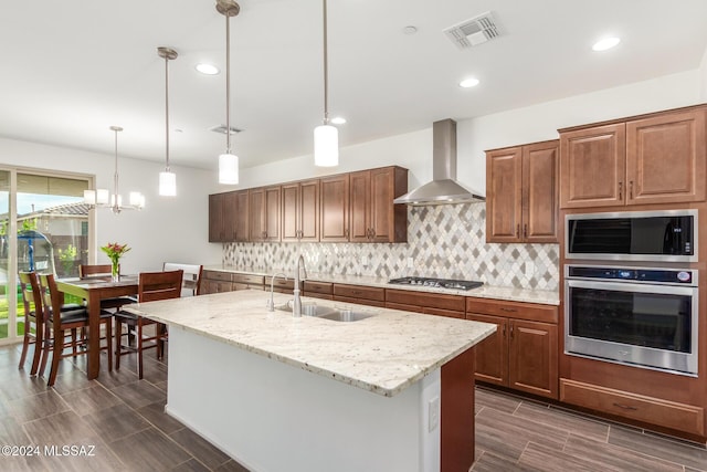 kitchen featuring sink, wall chimney exhaust hood, hanging light fixtures, and appliances with stainless steel finishes