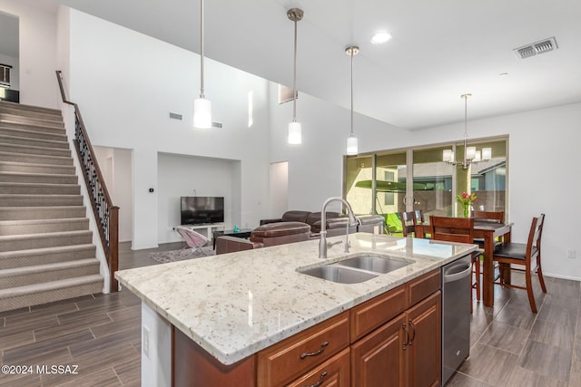 kitchen with stainless steel dishwasher, hanging light fixtures, sink, and a kitchen island with sink