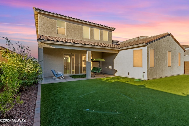 back house at dusk with a lawn and a patio area