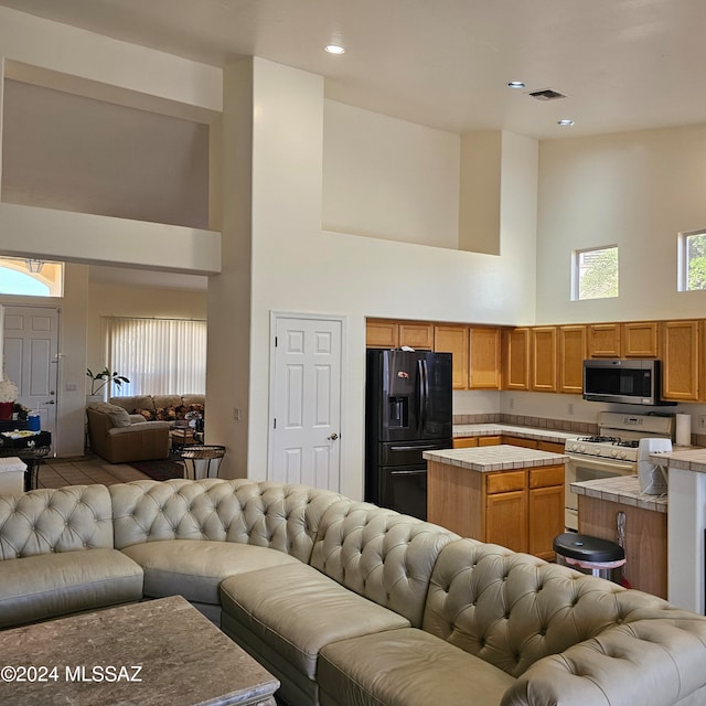 kitchen featuring a towering ceiling, tile countertops, white gas range oven, a center island, and black refrigerator with ice dispenser