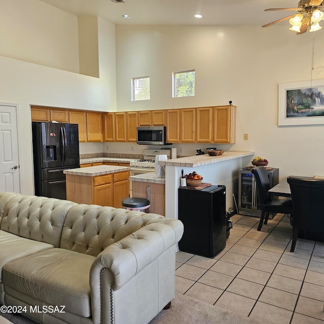 kitchen featuring fridge with ice dispenser, light tile patterned floors, white gas stove, high vaulted ceiling, and a center island