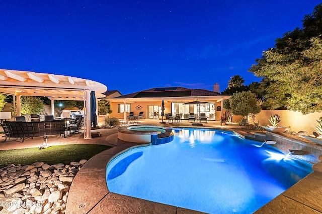 pool at night featuring a patio area, a pergola, and an in ground hot tub