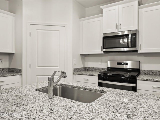 kitchen with white cabinetry, stainless steel appliances, light stone countertops, and a sink