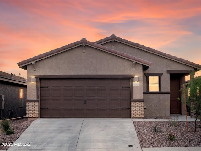 ranch-style home with driveway, stone siding, a garage, and stucco siding