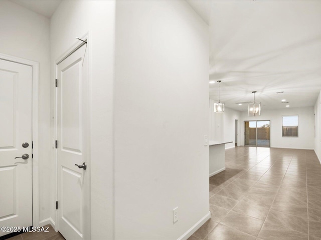 hallway featuring an inviting chandelier, tile patterned floors, and baseboards